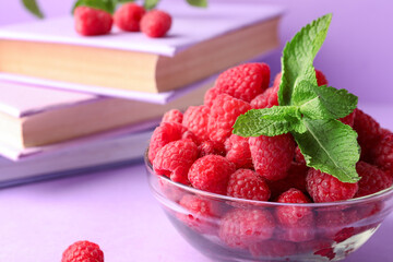 Glass bowl with fresh raspberries and books on lilac background