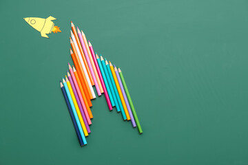 Pencils with paper rocket on green background