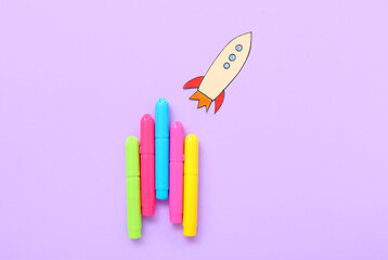 Markers with paper rocket on purple background
