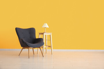 Stylish black armchair, wooden table and lamp near yellow wall