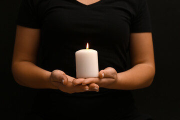 Woman holding burning candle on black background. National Day of Prayer and Remembrance for the Victims of the Terrorist Attacks.