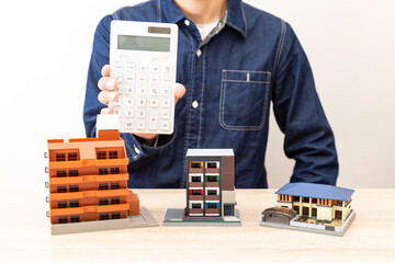 住宅模型の前で電卓を持つ男性