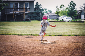 Obraz premium Young girl running to second base after a hit with dust coming up from the field. 