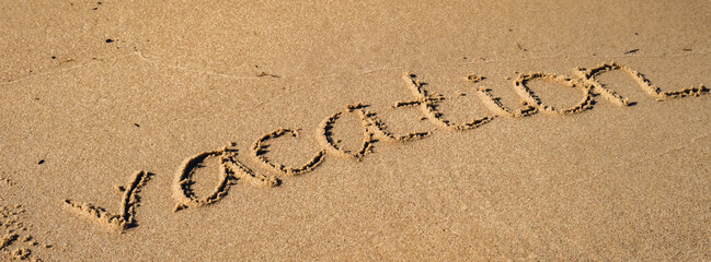 Text VACATION handwritten in sand surface. Blue ocean wave washing away message at the beach. Summer holidays beach writing vacation concept