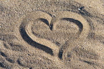 Drawing heart shape love concept on sand at the beach with vacation holiday summer travel background. Heart shape and footprint on sand.