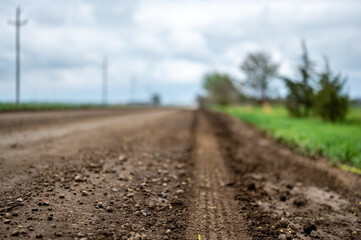 low angle view of a tire track left in a gravel road in a rural setting with spring green grass and...