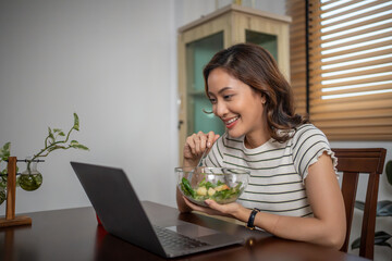 Woman eating healthy salad and working at home