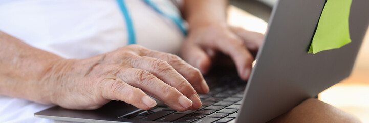 Old female hands typing on modern laptop