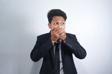 The Asian young man wearing suit, in shock, covers his mouth with his hands, thinking, No, this is impossible.