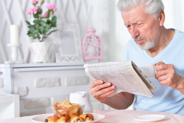 Emotional senior man reading newspaper at home