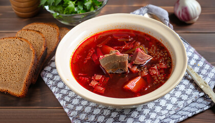 Borscht - Traditional Ukrainian dish. Vegetable soup made from beets, potatoes, cereals and boiled meat, and slices of rye bread in a ceramic bowl on a wooden kitchen table. Russian food cuisine