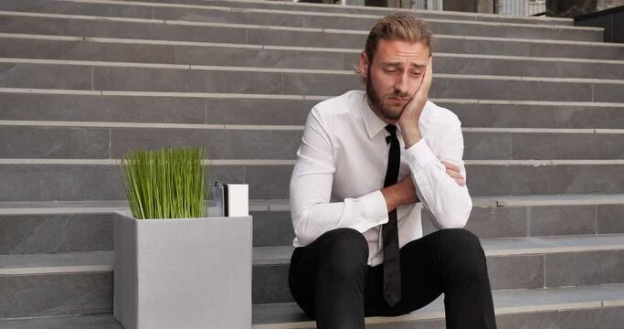 young buisness man in a shirt and tie sat on the steps looking sad and worried.