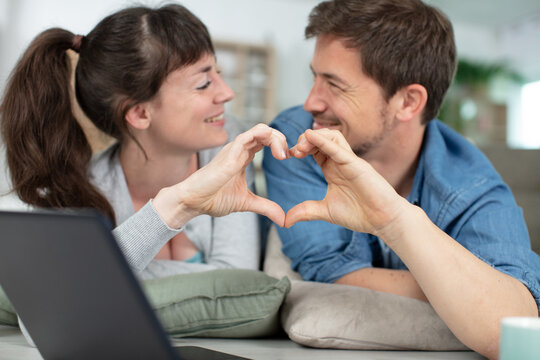 couple sitting using laptop doing heart symbol shape