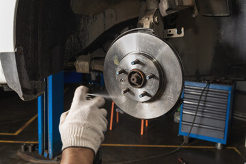 An auto mechanic uses an aerosol can to remove grease from a newly installed brake disc