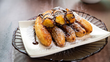 Fried banana dessert / Kluay Tod -Thai dessert with batter fried bananas dusted with powdered sugar and drizzled with chocolate glaze, selective focus