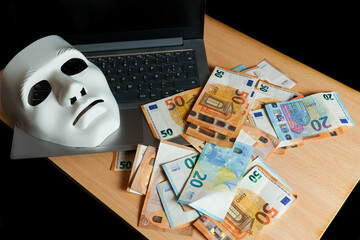 on a laptop there is a white mask and a pile of euro banknotes, cybercrime concept.