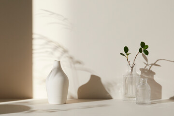 A room with various objects such as warm sunlight, shadows of grass leaves, a vase on a table, and cups