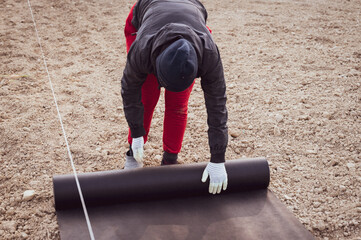 A woman spreads a roll of black agricultural fiber on the ground
