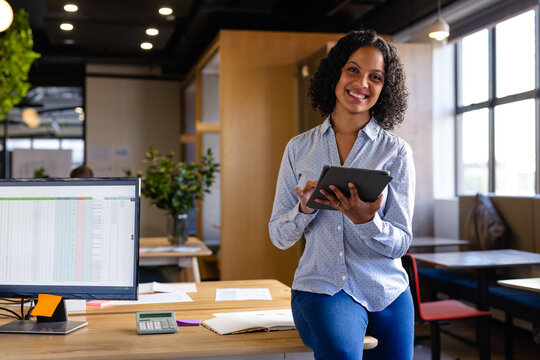 Portrait of happy biracial casual businesswoman using tablet in office