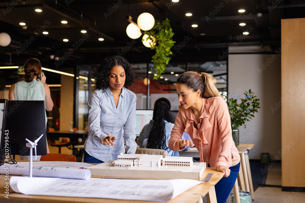 Wall mural diverse female architects in discussion using model and blueprints in casual office meeting