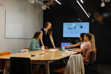 Diverse casual businesswomen in discussion using tablet and laptop in meeting room