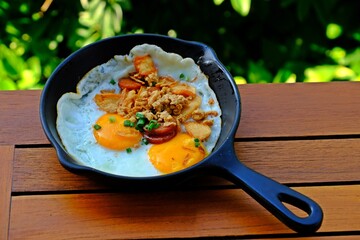 Indochina pan-fried eggs is fried egg topping with bacon and chinese sausage in hot pan.