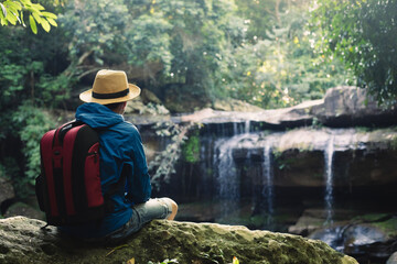 Backpacker sitting with beautiful waterfall, man wearing a hat with a waterfall,travel concept