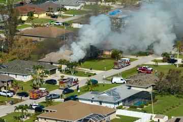 Burning residential house on fire with smoke and flames and firefighters extinguishing it after...