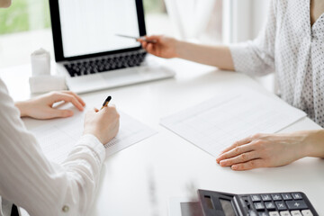 Two accountants using a laptop computer for counting taxes at white desk in office. Business Woman pointing into screen with a pen. Teamwork in business audit and finance