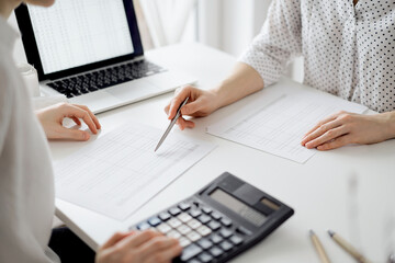 Accountant using a calculator and laptop computer for counting taxes with a client or a colleague...