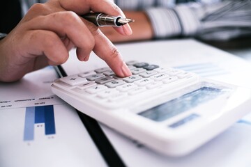 Business woman analyzing investment charts and pressing calculator buttons over documents. Accounting Concept.