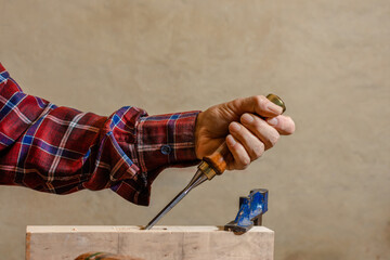 Close-up of the hand of a skilled craftsman holding a chisel as he firmly drives it into a piece of wood