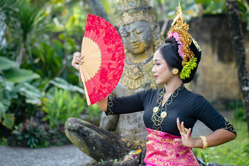 Woman poses in front of a Buddha statue in a costume and a crown in hair - obrazy, fototapety, plakaty