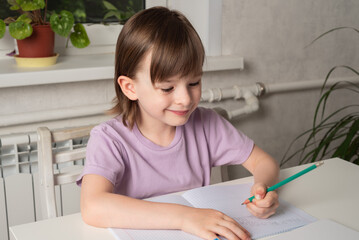 Happy girl sits at a table with books and a notebook and writes with her left hand. Left handed child. International Left Handers Awareness Day