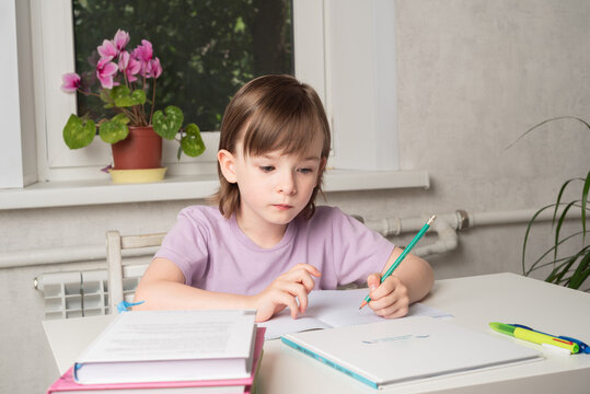 Girl sits at a table with books and a notebook and writes with her left hand. Left handed child.