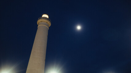 Lighthouse beam near the full moon in the night