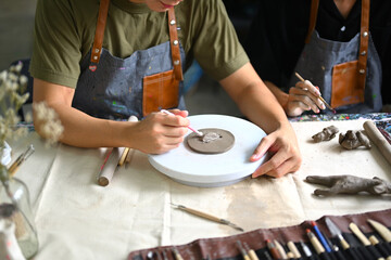 Craftspeople wearing aprons working with raw clay, shaping and decorating pottery in workshop