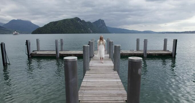 Young Woman In White Dress Walking In The Wooden Pier In Lake Lucerne, Switzerland. - aerial pullback