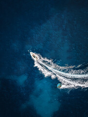 Aerial view of a motor speeboat towing a watersports fun inflatable tube over blue sea