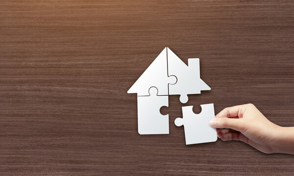 Close up picture of hands holding house jigsaw puzzle. build a house concept.