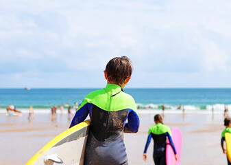 A child with a surfboard. Surfer school in summer, on a beach - obrazy, fototapety, plakaty