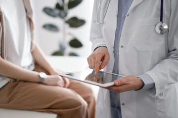 Doctor and patient in clinic. Friendly physician using tablet computer near a young woman. Medicine concept