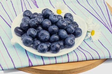 Fresh delicious sweet blueberries lie on a white decorative plate.