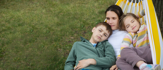 mom and Two kids  swing in a hammock in a summer park or garden. Concept of friendly family.