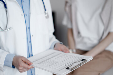 Doctor and patient discussing perfect health exam results. Friendly physician keeping with hands clipboard with medical papers near young woman. Medicine concept