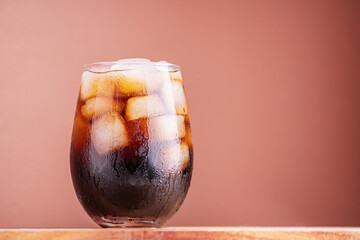 Brown soda, cold tea or coffee with ice cubes. Fresh cold sweet drink with ice cubes. Over brown background with copy space. Cola with ice. Fresh cold sweet drink with ice cubes.