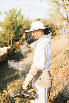 Male beekeeper with smoker working in apiary