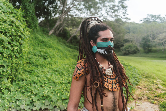 Ethnic man in painted face and braid standing in countryside