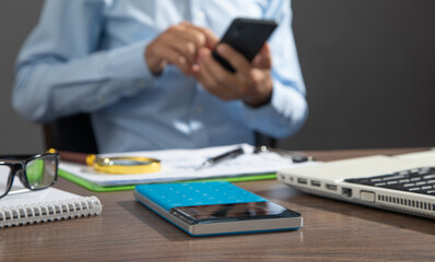 Fototapeta premium Focus on calculator with a man using smartphone.