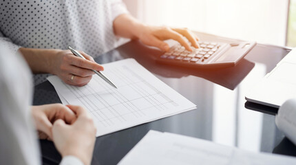 Woman accountant using a calculator and laptop computer while counting and discussing taxes with a client. Business audit and finance concepts